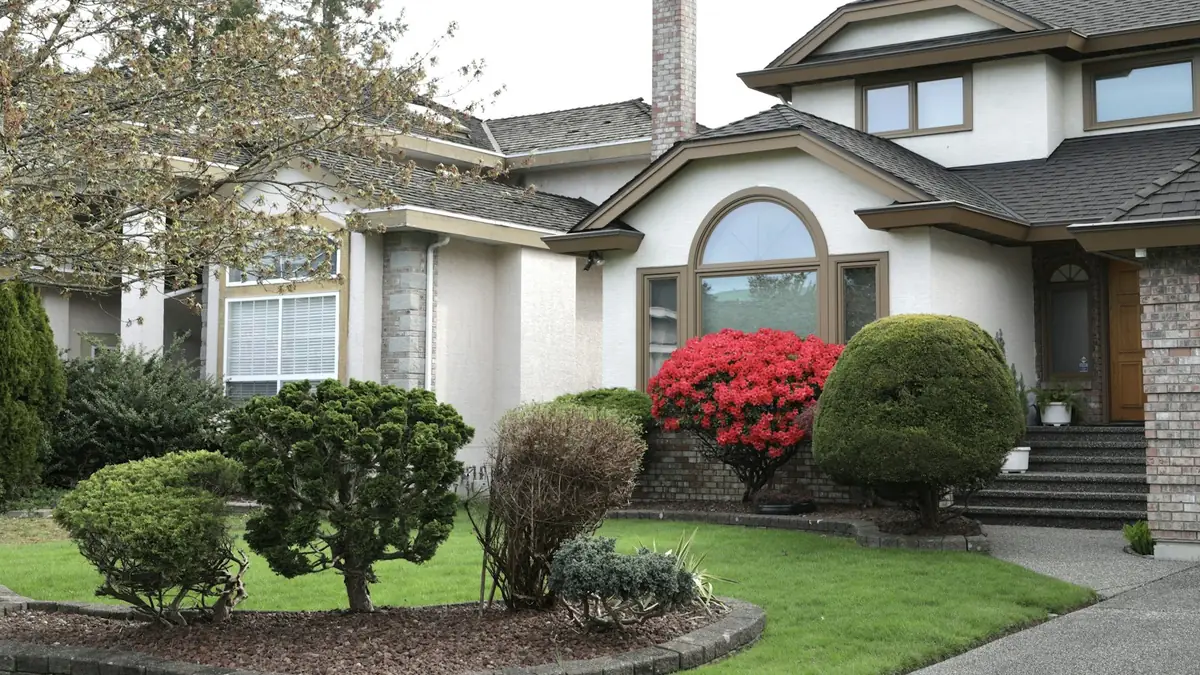 A stucco two-story house with red shrubs and a brick walk - Leak Detection in Commerce City